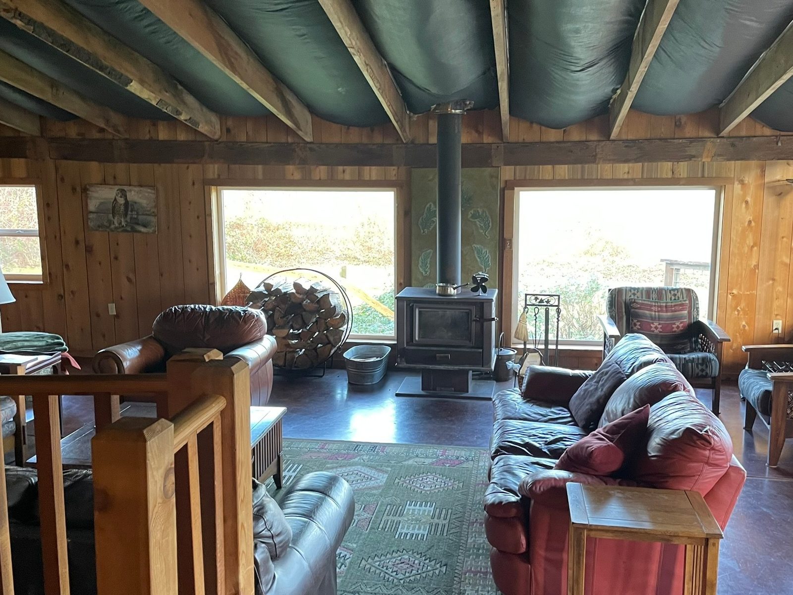 The lodge living room: cedar walls, exposed beams, a wood stove between two big windows, and couches around a rug