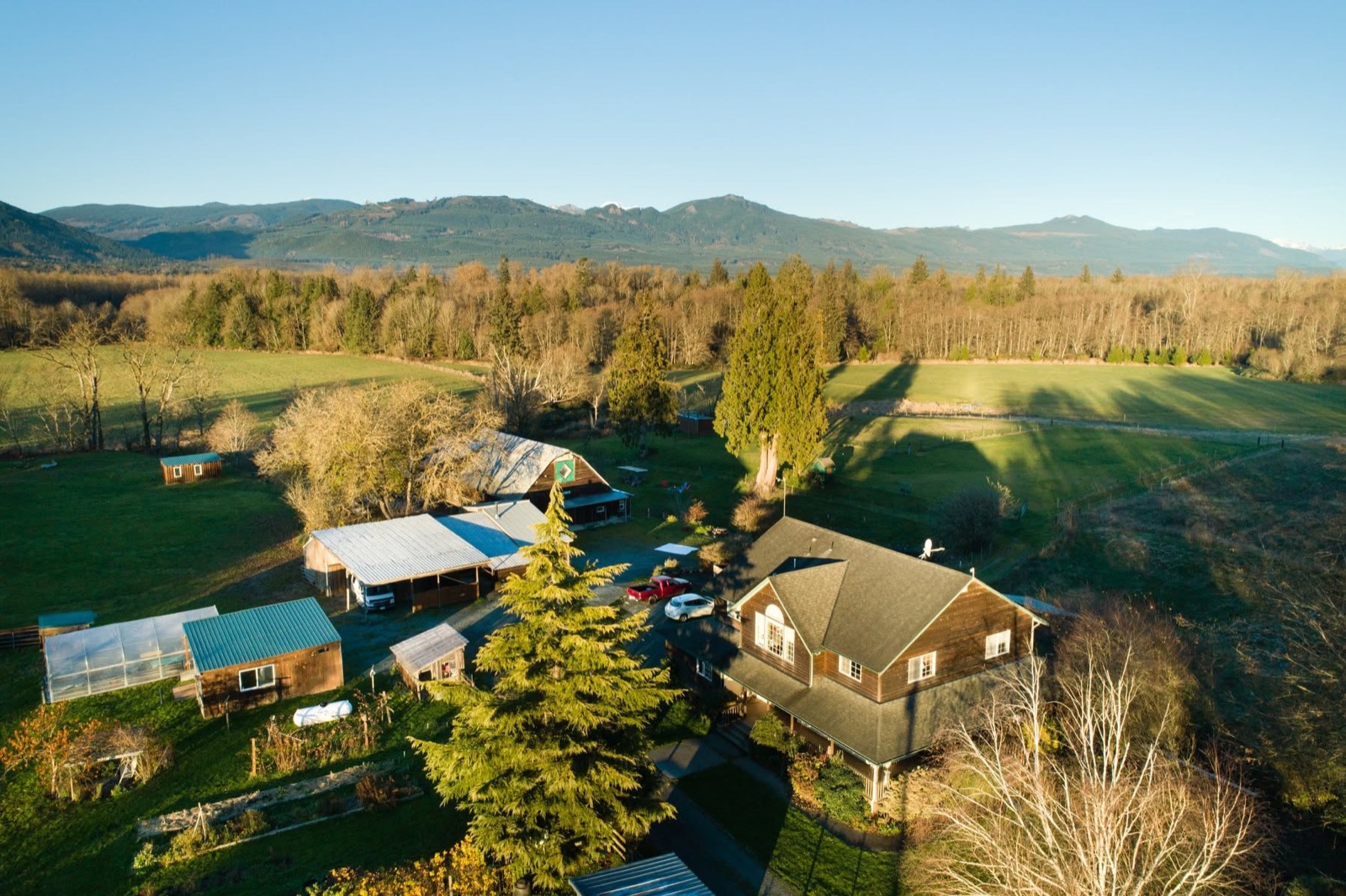 Aerial view of the lodge, outbuildings, gardens, and fields, with forest and mountains beyond